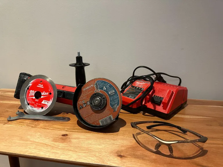 Meuleuse sans fil Milwaukee avec disques de coupe, chargeur, clé de serrage et lunettes de protection sur table en bois