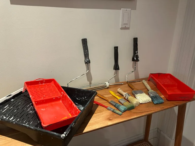 Kit de peinture complet avec rouleaux, pinceaux de différentes tailles et bacs à peinture rouges et noirs, posés sur une table en bois